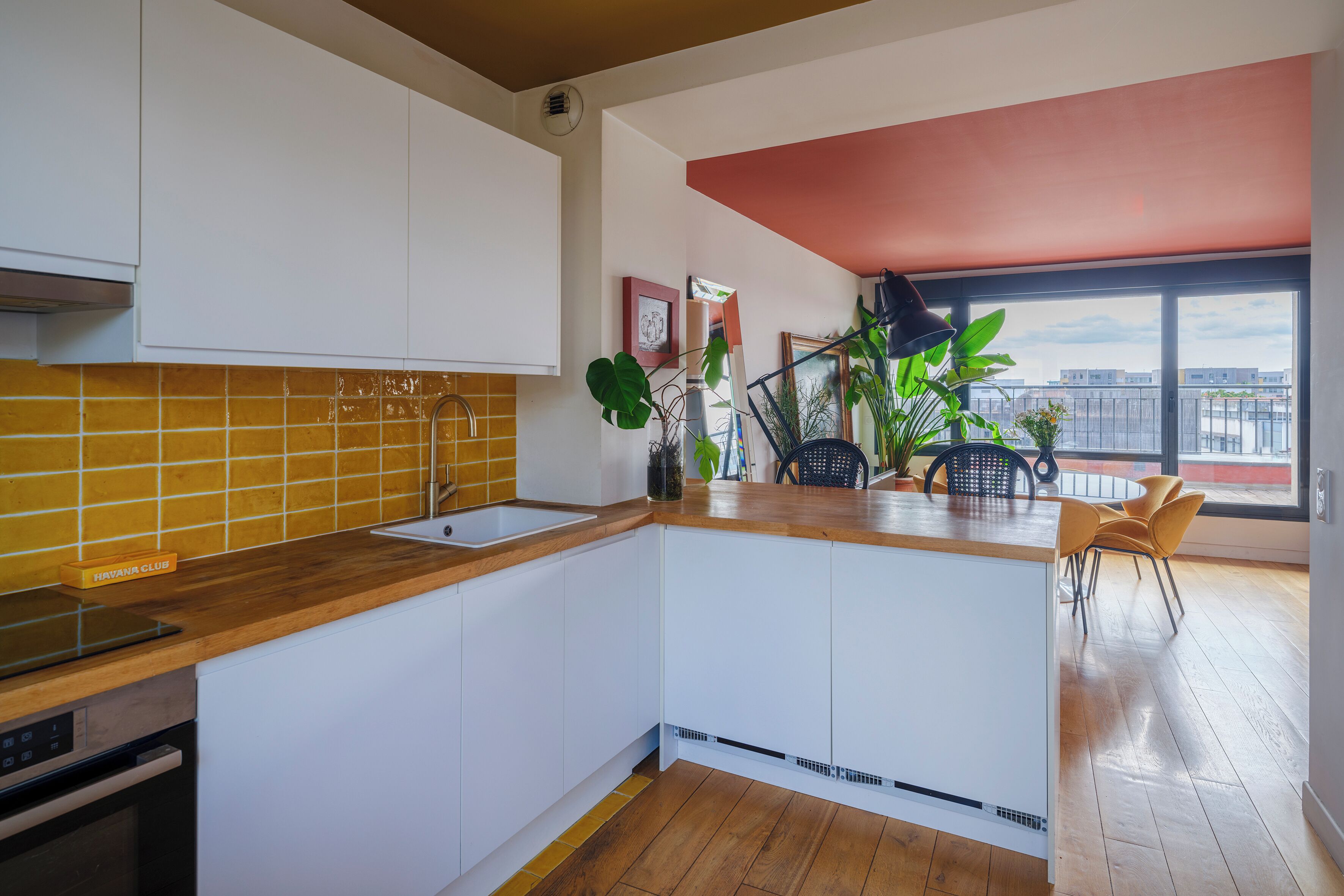 Une cuisine moderne avec un plan de travail en bois, des armoires blanches et un dosseret carrelé de carreaux jaunes.