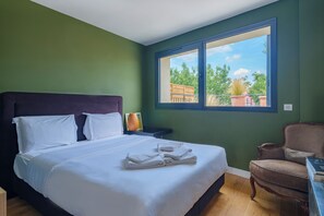 Ein Hotelzimmer mit einem großen Bett, einem Sessel und einem Fenster mit Blick auf Grünflächen.