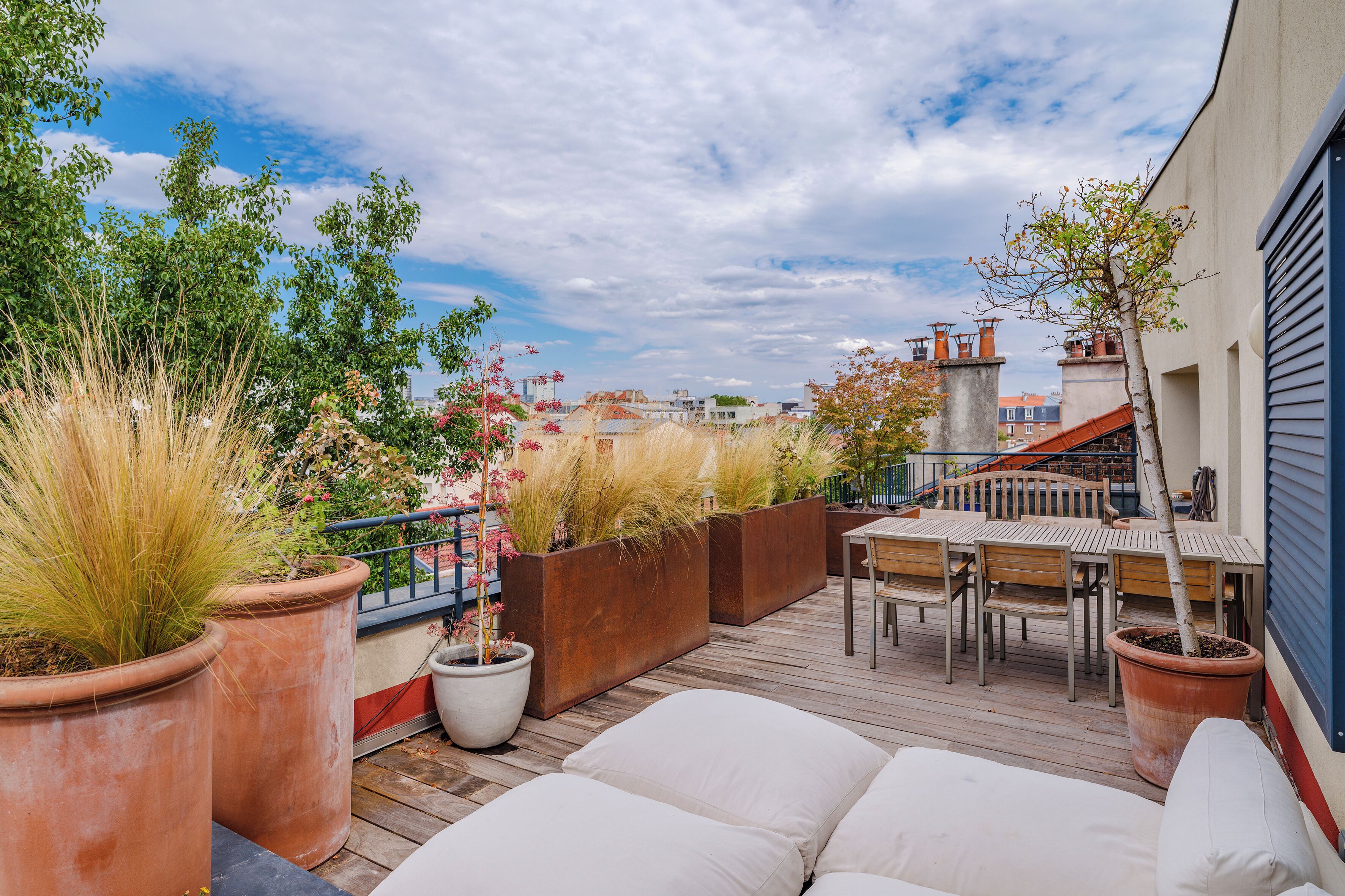 A rooftop terrace with outdoor seating, potted plants, and a view of the cityscape.