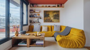 Un salon moderne avec un canapé jaune, une table basse sur laquelle sont posés des livres et un tableau accroché au mur.
