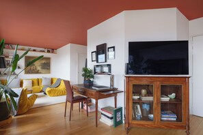 Ein Wohnzimmer mit Holzboden, einem gelben Sofa, einem Schreibtisch mit Computer und einem Bücherregal.
