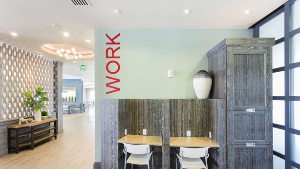 Een modern interieur met een 'WORK' bord, houten vloeren, twee witte stoelen, een houten kast en een decoratieve wand.