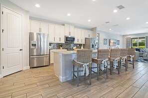 A modern kitchen with stainless steel appliances, a built-in microwave, and a large island with bar stools. - The Encore Bliss -  Luxury 9-Bed Villa with Oversized Pool & Spa (Kissimmee)