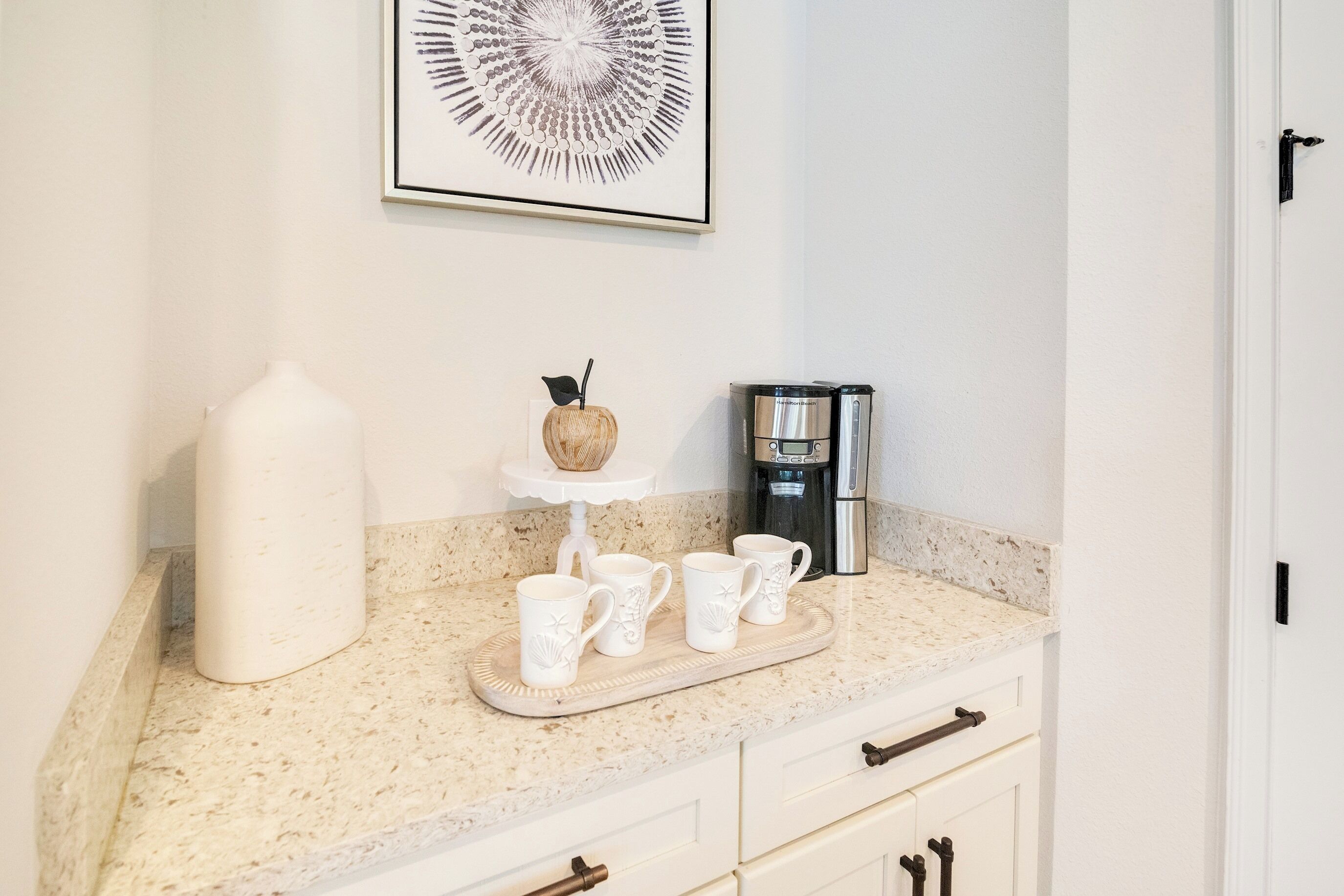A kitchen counter with a coffee maker, a decorative item, and a tray with cups.