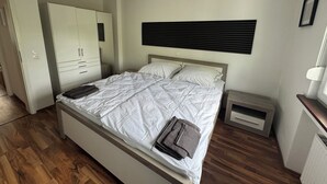 Ein Schlafzimmer mit einem Bett, einem Kleiderschrank, einem Nachttisch und einem Beistelltisch.