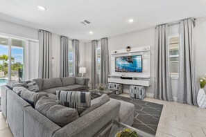 A modern living room with a grey sectional sofa, a flat-screen TV mounted on the wall, a glass coffee table, and a patterned rug. - Silver Sands Villa - Eight Bedroom Apartment, Sleeps 10 (Kissimmee)