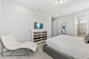 A modern bedroom with a bed, a white chair, a TV, and a walk-in closet. - Silver Sands Villa - Eight Bedroom Apartment, Sleeps 10 (Kissimmee)