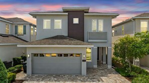 Une maison moderne à deux étages, dotée d’un garage, d’une grande fenêtre et d’une allée pavée en briques.