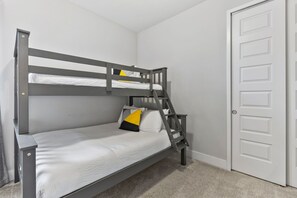 Una cama litera con escalera, ropa de cama blanca y una almohada amarilla.