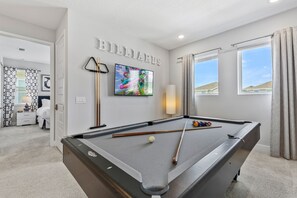 Ein Billardtisch mit Billardkugeln und Spielstöcken, ein Billardständer und ein an der Wand befestigter Fernseher.