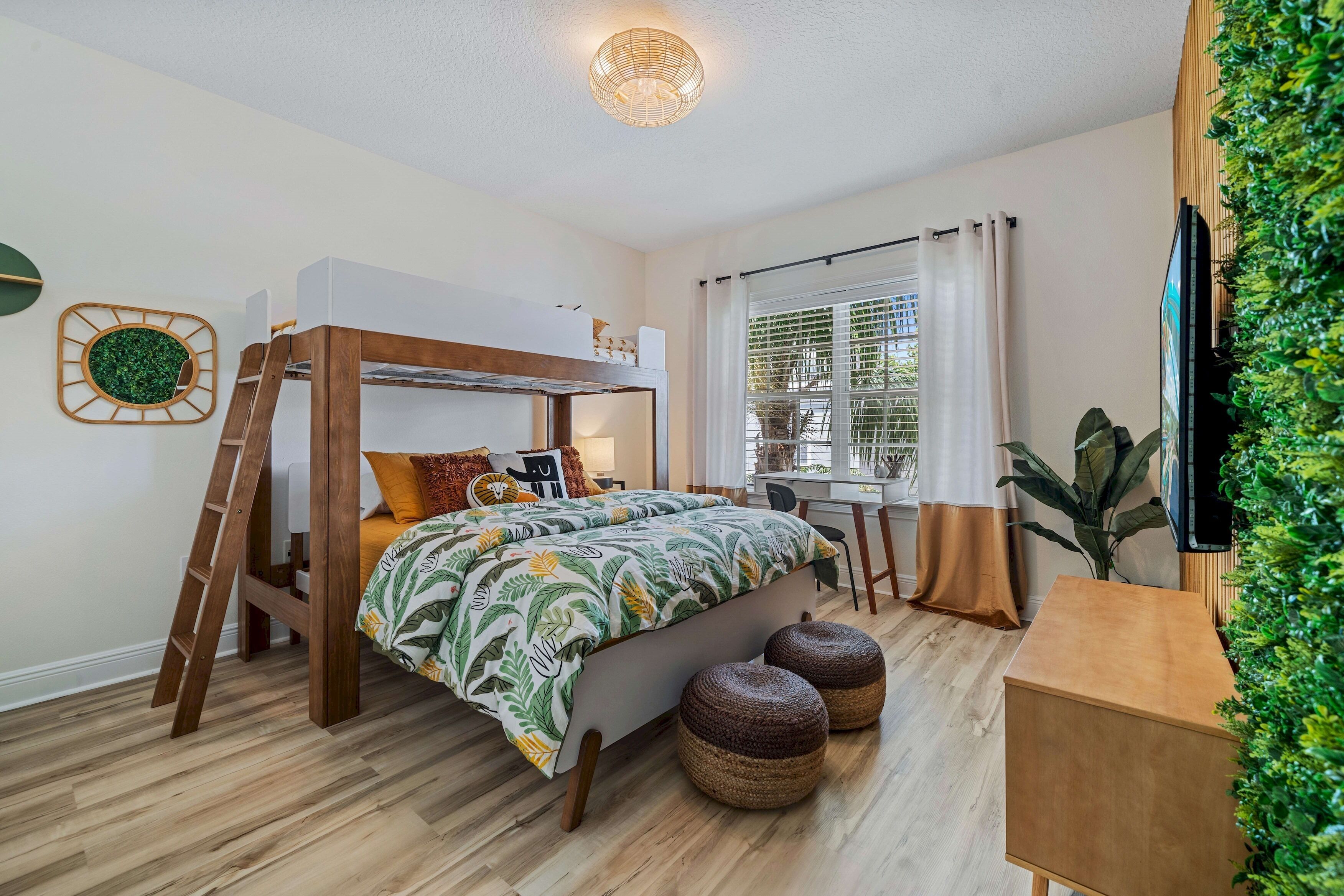 A bedroom with a bunk bed, a desk, a chair, and a large window with curtains.