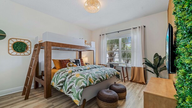 Ein Schlafzimmer mit Etagenbett, Schreibtisch, Stuhl und einem großen Fenster mit Vorhängen.