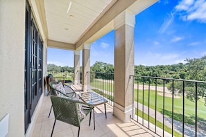 A covered balcony with a table and chairs, overlooking a well-maintained lawn and trees. - Summer Breeze - Four Bedroom Villa, Sleeps 8 (Kissimmee)