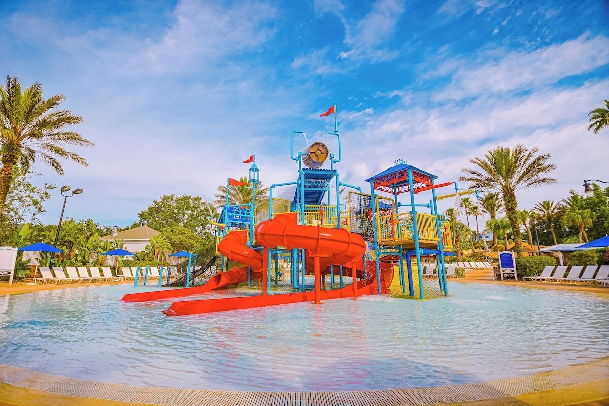Ein Wasserpark mit einer zentralen roten Wasserrutsche, einem Glockenturm und einer blau-gelben Spielanlage.