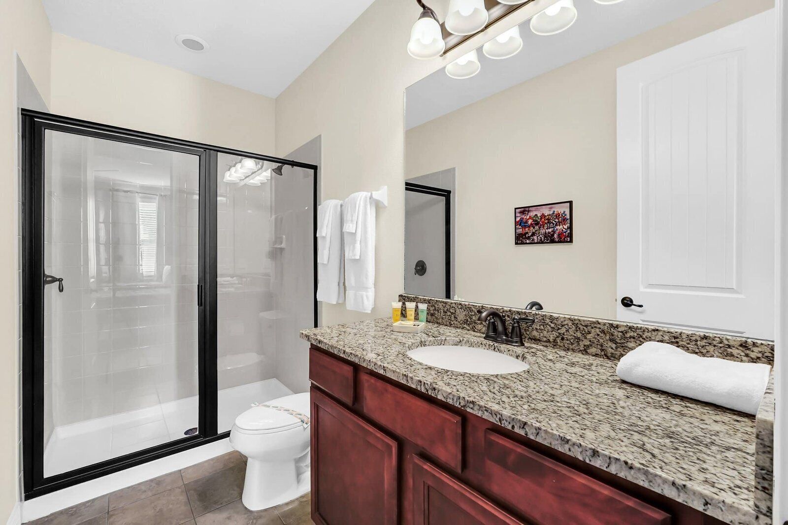 A modern bathroom with a glass-enclosed shower, a white toilet, a granite countertop with a sink, and a large mirror.