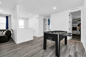 Een moderne woonkamer met een tafelvoetbaltafel, een bank en een deur naar een andere kamer.