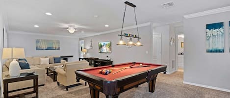 A living room with a pool table, a sofa, a TV, and a ceiling fan.