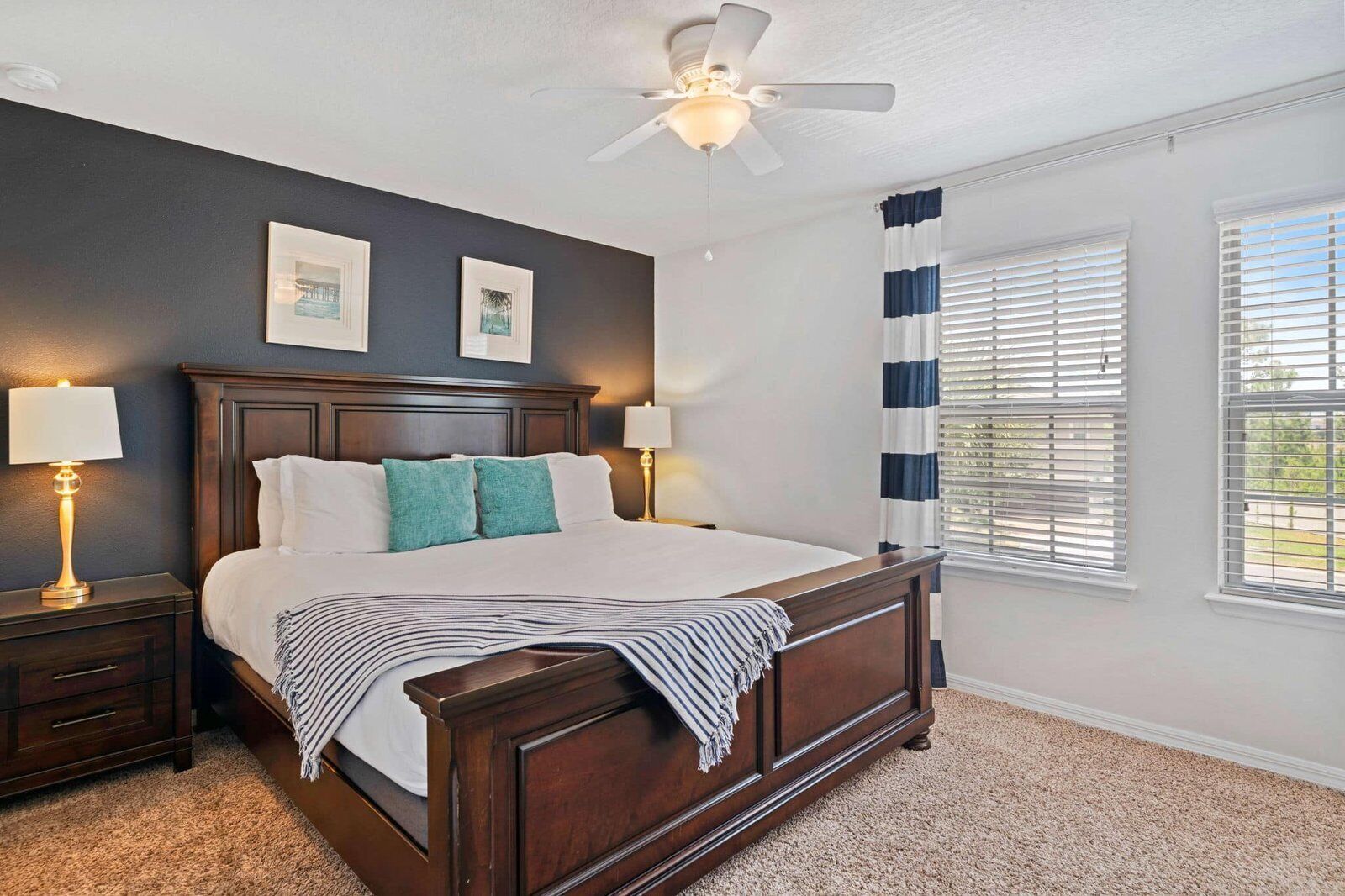 A bedroom with a large bed, two bedside lamps, a ceiling fan, and a window with blinds.