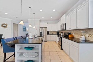 Une cuisine moderne avec des meubles blancs, un îlot central et des luminaires suspendus.