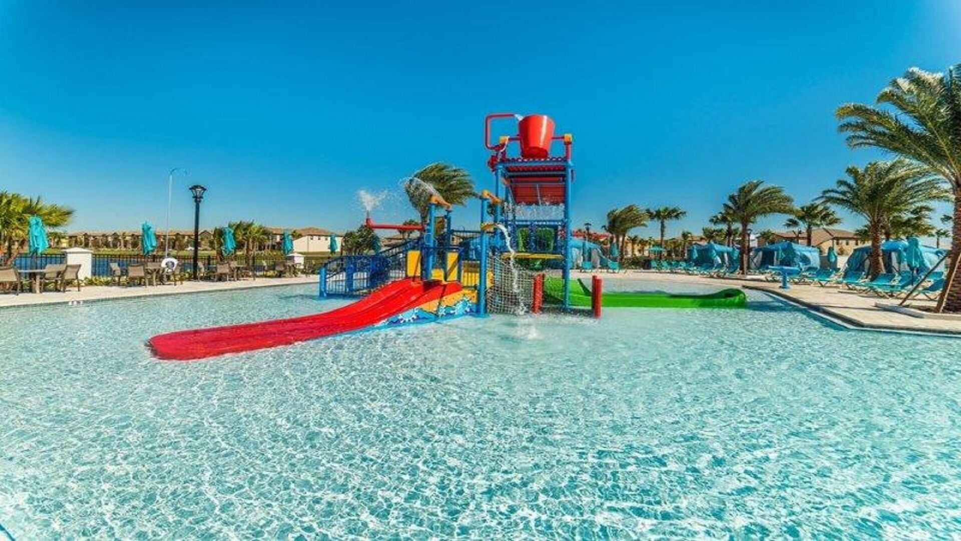 Een waterpark met een rode glijbaan, een speelstructuur en helderblauw water.
