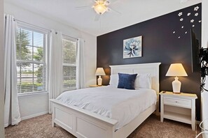 Ein Schlafzimmer mit einem weißen Bett, zwei Nachttischen mit Lampen, einem Deckenventilator und einem Fenster mit Vorhängen.