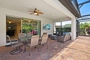 Une terrasse extérieure avec une porte vitrée donnant sur un coin repas, des meubles en osier et un ventilateur de plafond.