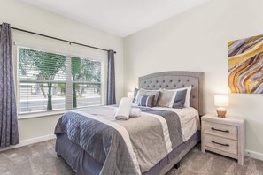 A bedroom with a bed, bedside tables, a window with curtains, and a wall-mounted artwork. - Birdie Bungalow - Four Bedroom House, Sleeps 8 (Kissimmee)