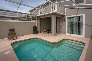Ein Schwimmbecken mit überdachtem Patio, einem Stuhl und einem Tisch.