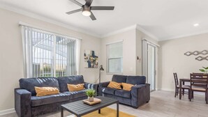 A modern living room with two sofas, a coffee table, and a dining area with chairs. - Birdie Bungalow - Four Bedroom House, Sleeps 8 (Kissimmee)