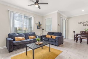 A modern living room with two sofas, a coffee table, and a dining area with chairs. - Birdie Bungalow - Four Bedroom House, Sleeps 8 (Kissimmee)