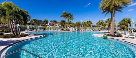 A large outdoor swimming pool with clear blue water, surrounded by palm trees and lounge chairs.