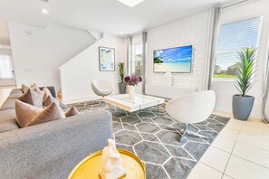 Ein modernes Wohnzimmer mit einer Couch, Sesseln, einem Couchtisch und einem Fernseher.