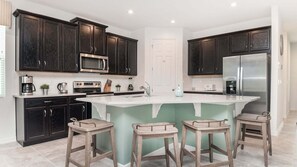 Cocina moderna con armarios de madera oscura, electrodomésticos de acero inoxidable, una isla central con taburetes y una puerta blanca.