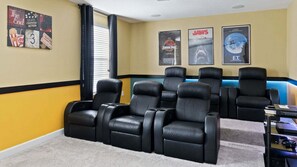 Una sala de cine en casa con seis sillones reclinables de cuero negro, una pantalla grande y carteles de películas en la pared.