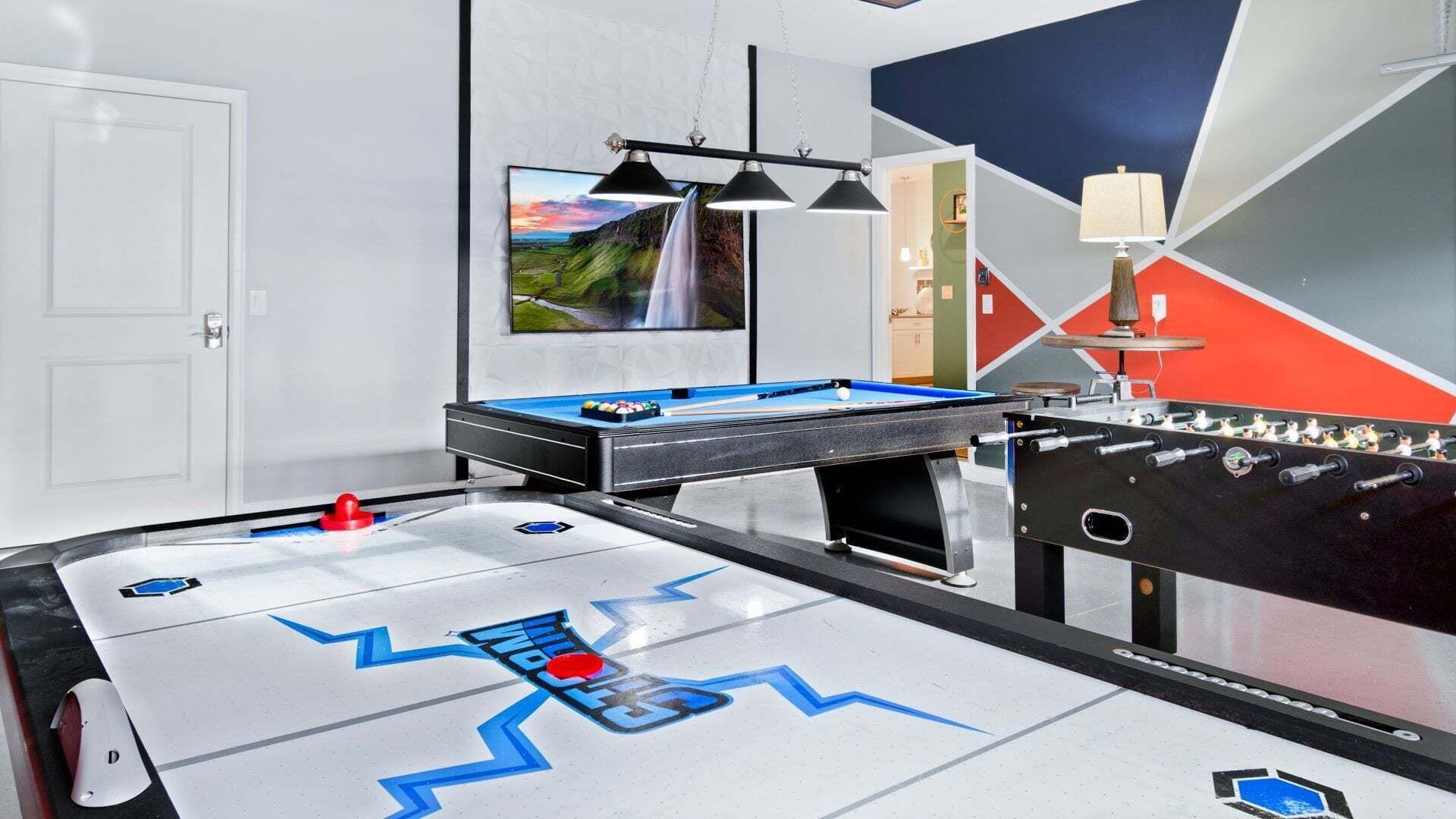 A room with a pool table, foosball table, and a painting on the wall.