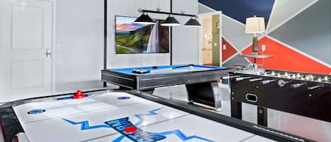 Une pièce équipée d’une table de billard, d’un baby-foot et ornée d’un tableau au mur.