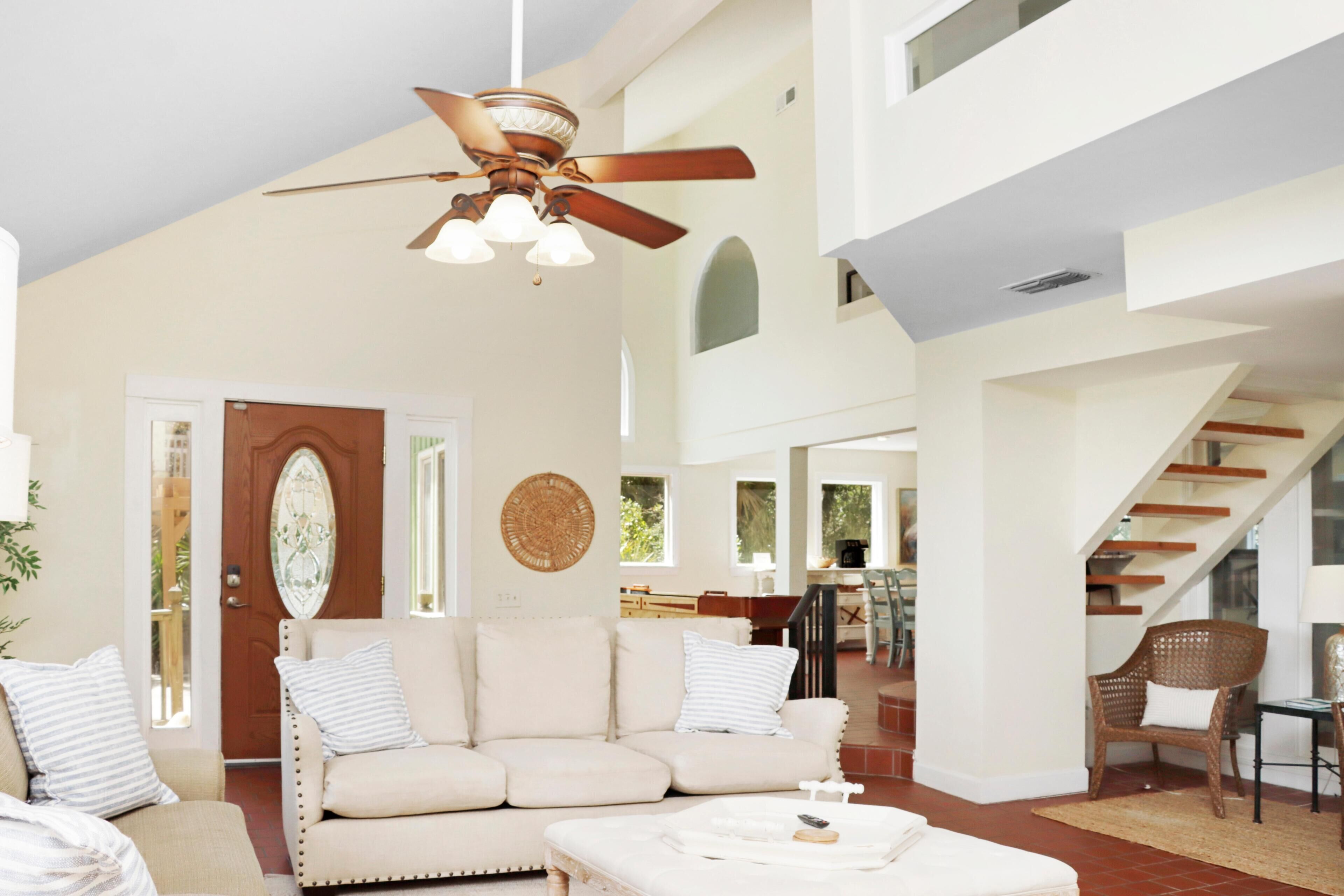 A spacious living area with a high ceiling, a ceiling fan, a sofa set, and a staircase leading to an upper level.