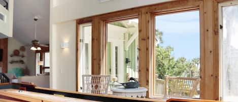 A room with a wooden bench, a table, and a large window with a view of greenery.