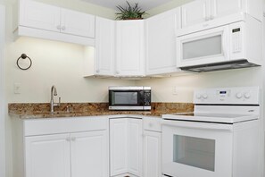 A compact kitchen with white cabinetry, a microwave, an oven, and a granite countertop. - Hidden Palms (Port St. Joe)