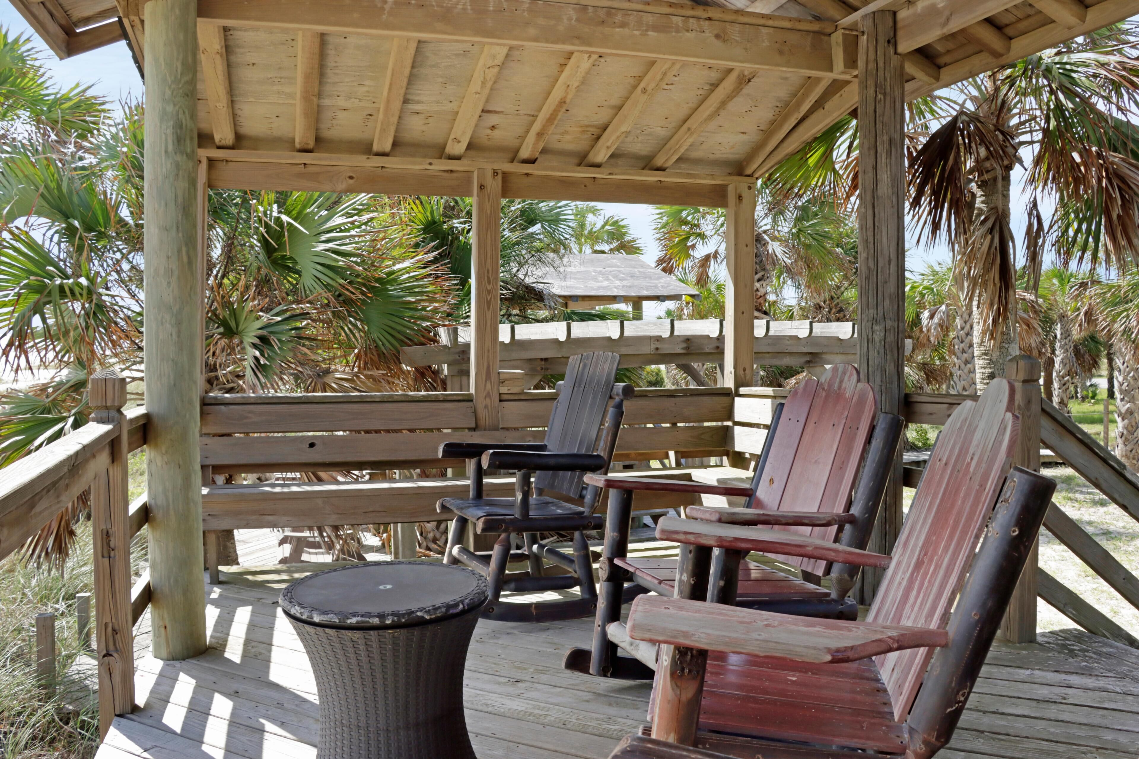 Een houten terras met een overdekte zithoek, inclusief een tafel en stoelen.