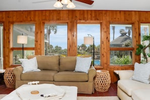 A room with a wooden paneled wall, a beige sofa with striped pillows, a white coffee table, and two side tables with lamps. - Hidden Palms (Port St. Joe)