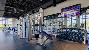 Un gimnasio con diversos equipos de ejercicio, una pantalla grande de televisión y un espejo.