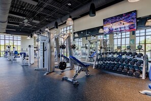 A gym with various exercise equipment, a large TV screen, and a mirror. - Island Vibes - Five Bedroom House, Sleeps 12 (Kissimmee)