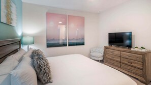 A bedroom with a bed, a TV on a wooden dresser, a chair, and two wall-mounted paintings. - Island Vibes - Five Bedroom House, Sleeps 12 (Kissimmee)