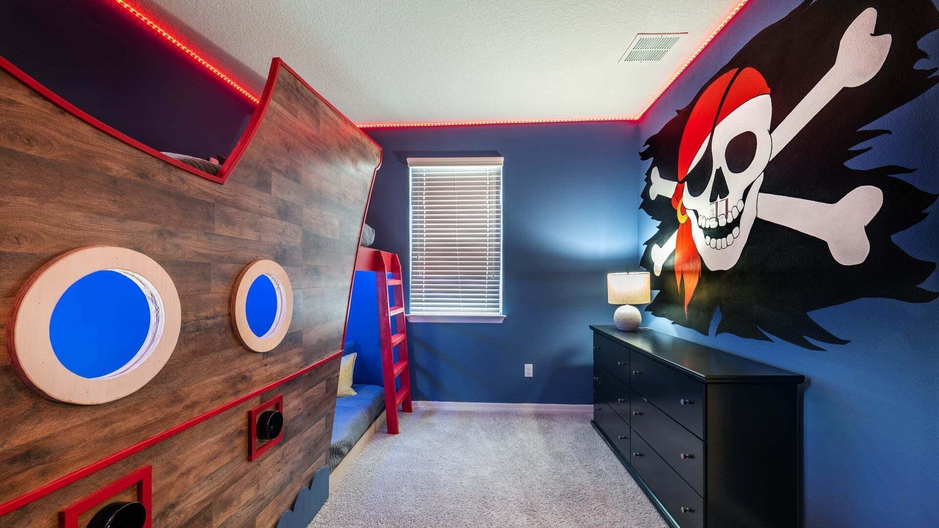 A room with a wooden wall, a window with blinds, a desk with drawers, and a wall with a pirate-themed mural.