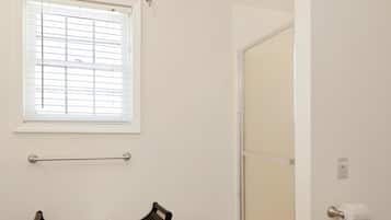 A bathroom with a shower, a towel rack, and a window with blinds.