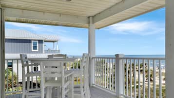 A covered outdoor area with a table and chairs, overlooking a beach and a house.