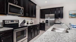 A modern kitchen with dark cabinetry, stainless steel appliances, and a granite countertop. - Maison Calme - Five Bedroom Villa, Sleeps 13 (Kissimmee)