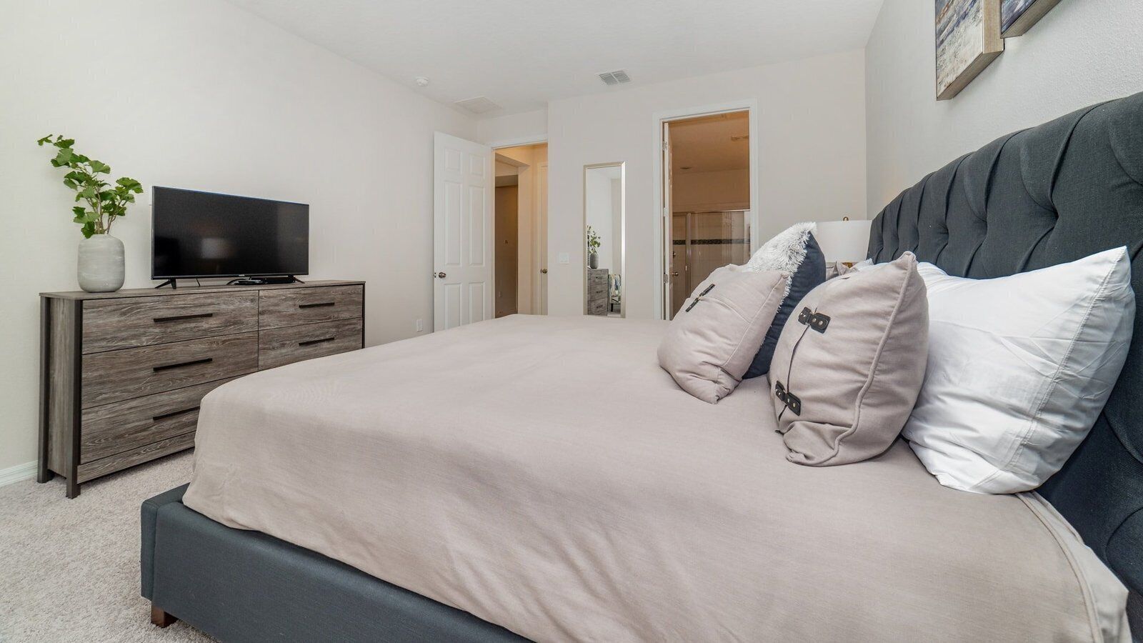 A bedroom with a bed, a television on a wooden dresser, and a door leading to another room.