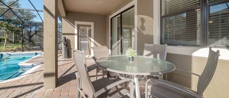 A patio with a glass table and chairs, a pool, and a covered area with a door and windows.